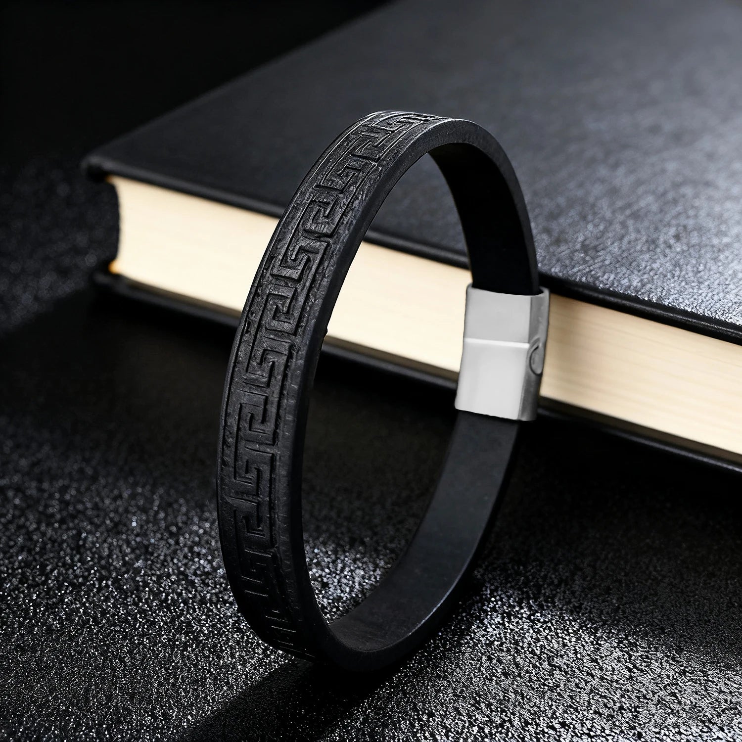 Black leather bracelet with metallic clasp on a book