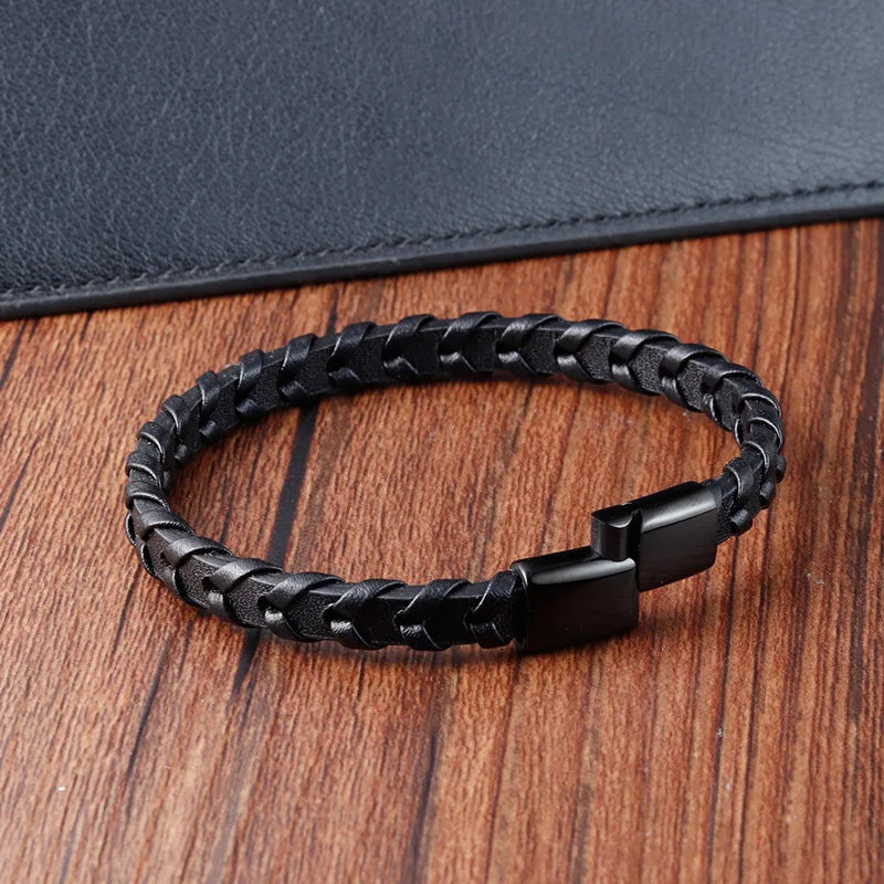 Black braided leather bracelet on a wooden surface with a dark blue fabric background