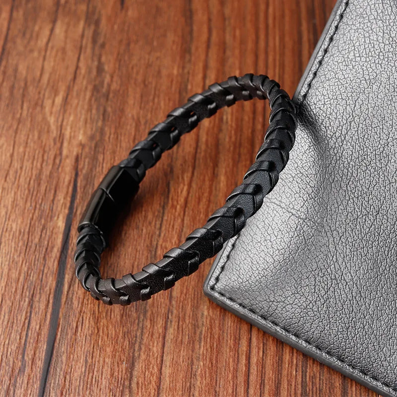 Black braided leather bracelet on a wooden surface with a gray textured object.